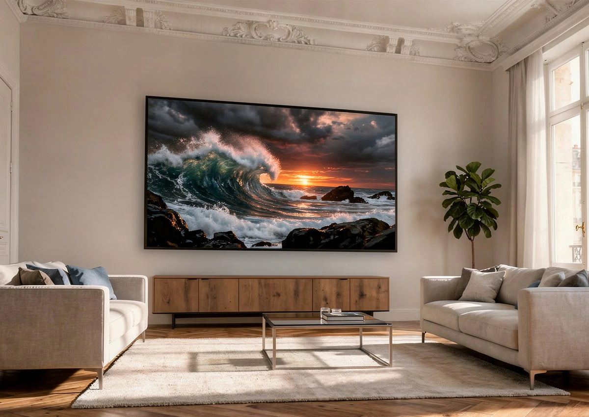 The image shows an elegant living room with two sofas and a celexon HomeCinema High Contrast Frame Projector Screen – Dynamic Slate ALR, displaying a powerful ocean wave at sunset.