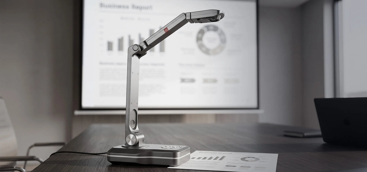 A modern meeting room with a celexon DK500 document camera on a conference table; next to it is a business report whose contents are displayed on a large projection screen in the background.