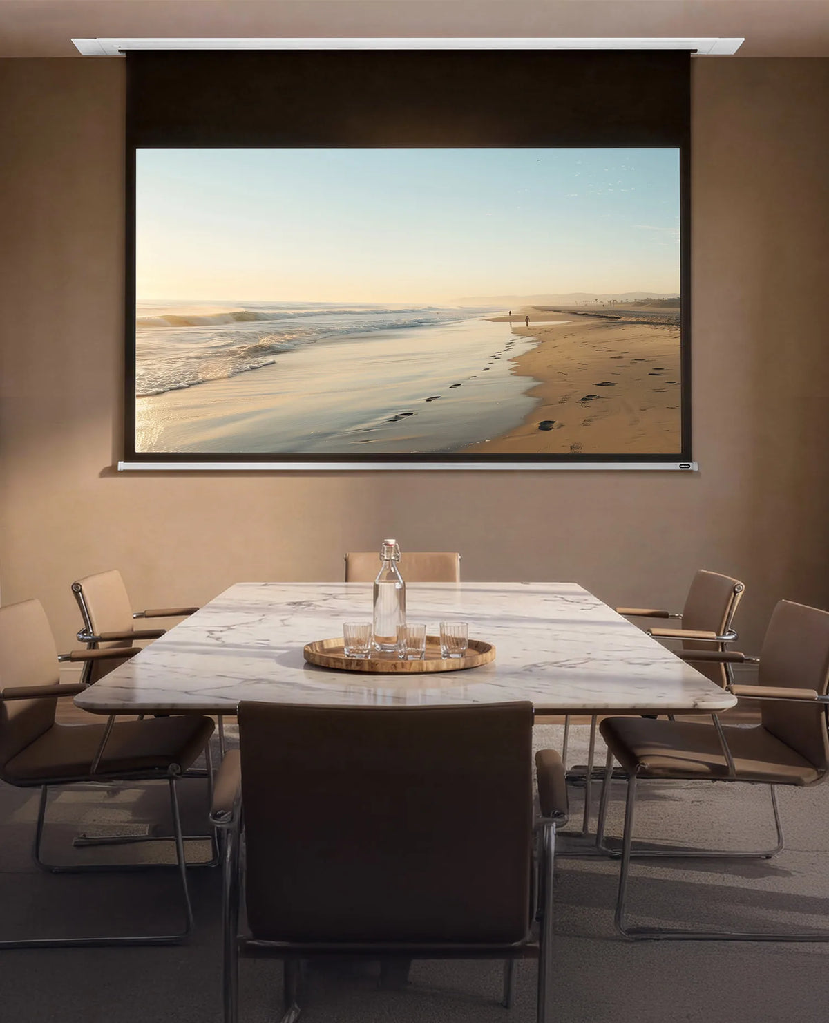 An elegant meeting room with floor-to-ceiling windows overlooking classic city façades. At the center stands a rectangular marble table surrounded by modern chairs. A celexon Ceiling Recessed Electric Professional Plus projector screen is integrated into the ceiling, displaying a calm beach scene with sea, sand, and footprints in warm morning or evening light.