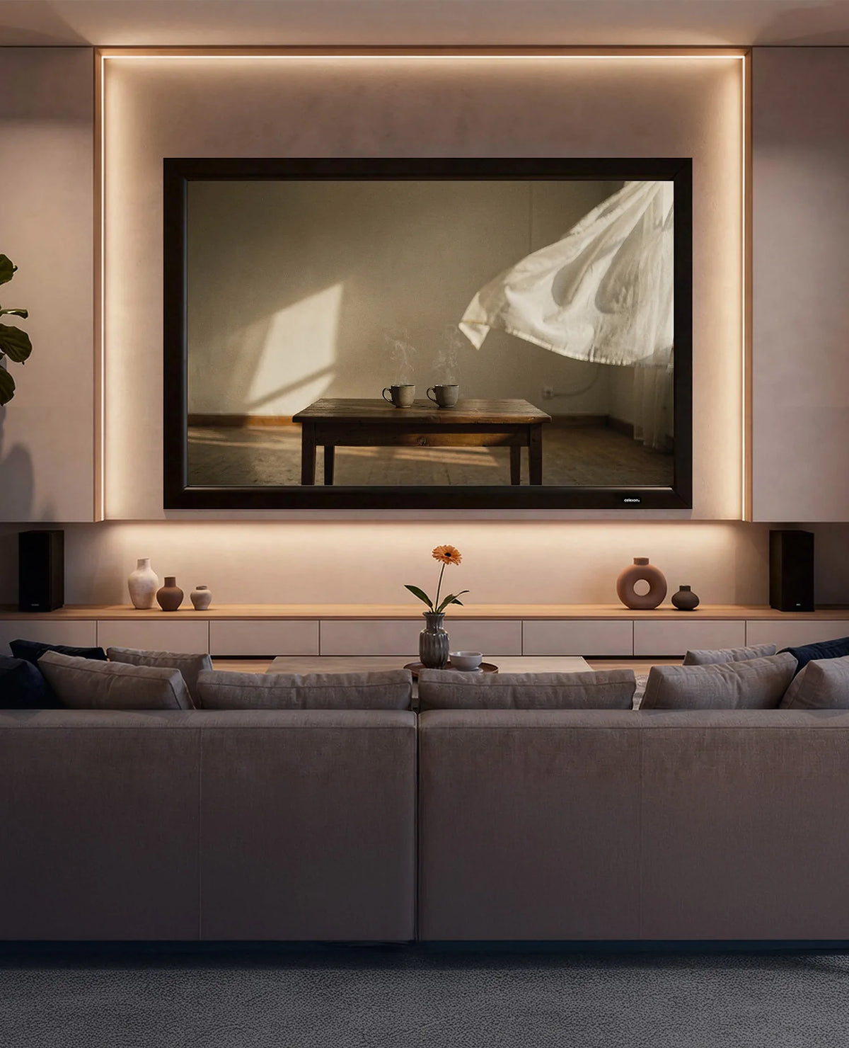 The image shows a modern, atmospherically lit living room with a celexon Home Cinema fixed-frame projector screen displaying two coffee cups on a wooden table. Overall, a calm evening atmosphere prevails, and the room offers a wide view over a cityscape through floor-to-ceiling windows.
