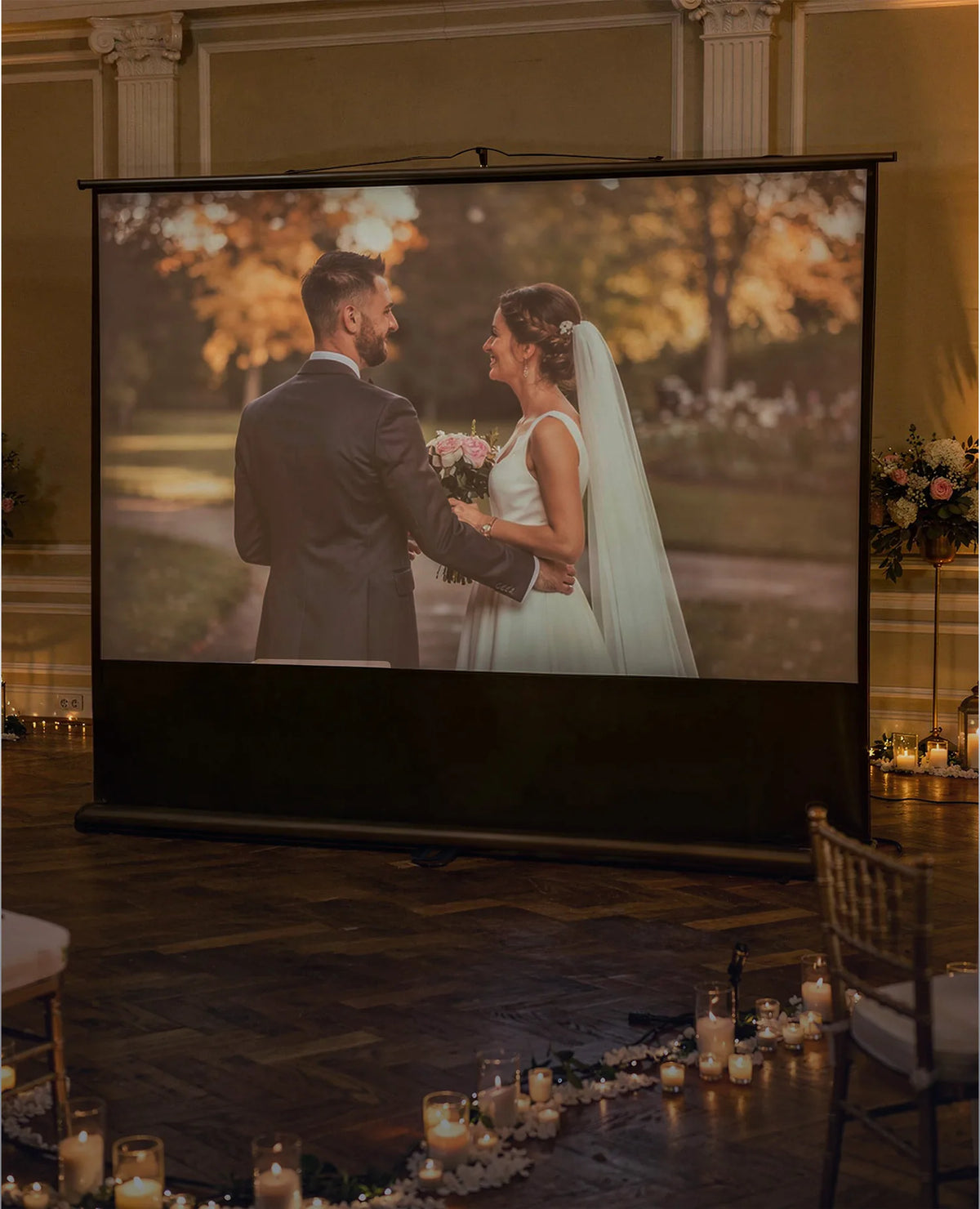 Elegant banquet hall featuring a celexon Ultramobile Professional projector screen, on which a romantic wedding photo of the bridal couple is atmospherically projected.