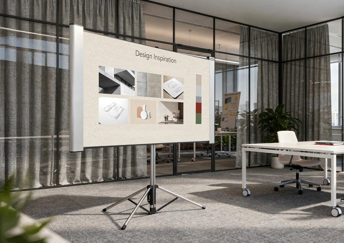 The image shows a modern workspace or creative studio with glass walls and open office structures. At the center stands a celexon Dual Format Tripod Screen Mobile Expert displaying a presentation titled “Design Inspiration,” consisting of various material, architecture, and design examples as well as a color palette.