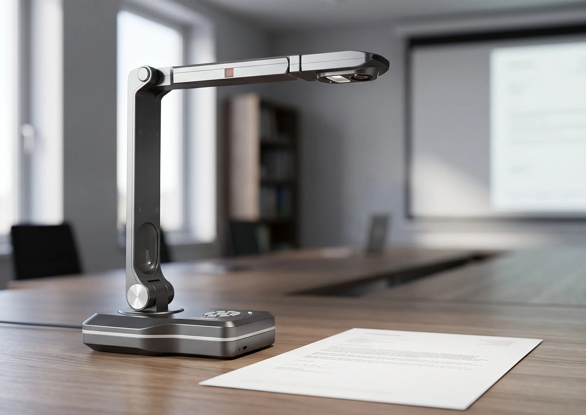A modern celexon DK800 document camera on a conference table next to a document; in the background, a meeting room and projection screen are visible out of focus.