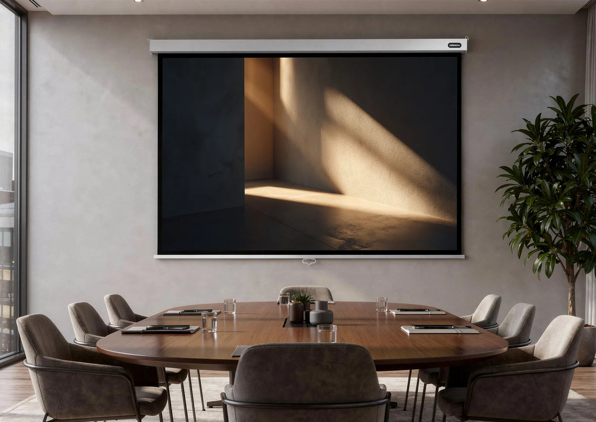 A modern conference room with a large wooden table, upholstered chairs, and floor-to-ceiling windows; mounted on the wall is a celexon Manual Professional Plus projector screen displaying a minimalist light-and-shadow motif, alongside a tall indoor plant and a city view.