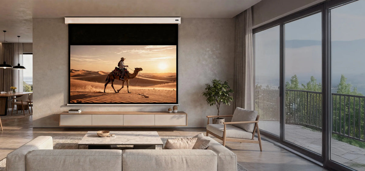 A modern living room with a celexon Electric Professional Plus V2.0 Battery projector screen. Displayed on it is a warm desert scene at sunset: a person riding a camel through sand dunes.