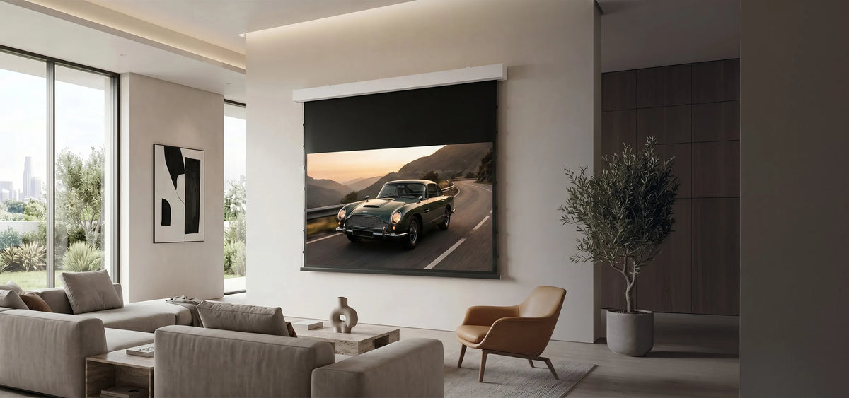 A modern living room featuring a celexon DARKVISION ALR Premium Plus Screen Electric Tension, displaying a classic sports car on a winding mountain road. Light-colored seating, a leather armchair, and a large indoor plant complement the elegant, minimalist interior.