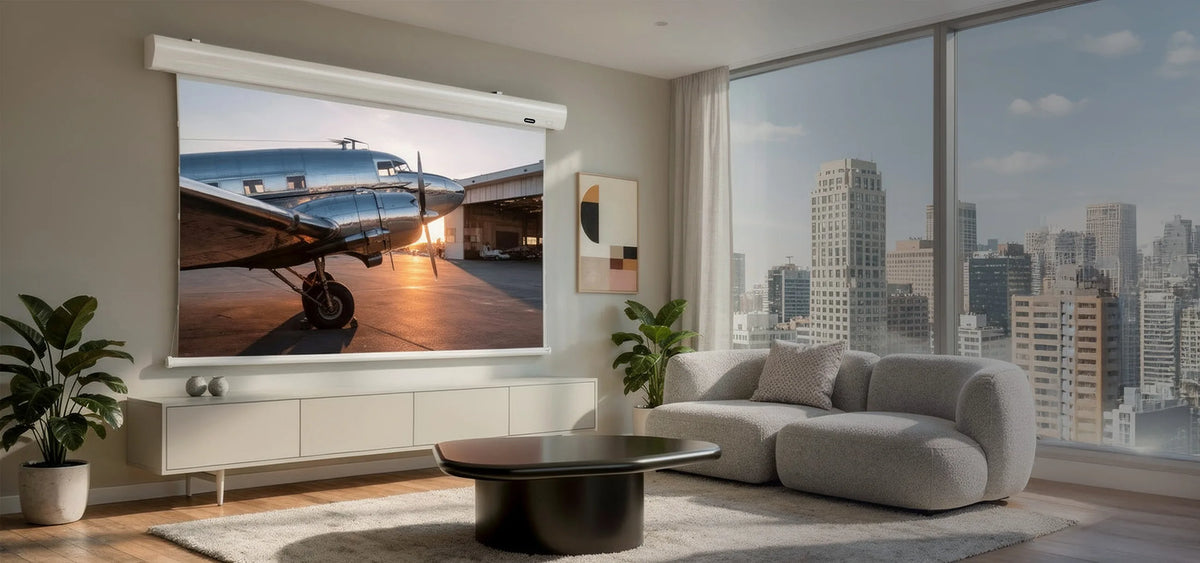 Modern, bright living room with floor-to-ceiling windows and a city view, featuring an elegant celexon HomeCinema High Contrast Frame Projector Screen – Dynamic Slate ALR displaying an atmospheric projection of a nostalgic propeller aircraft in warm sunlight.