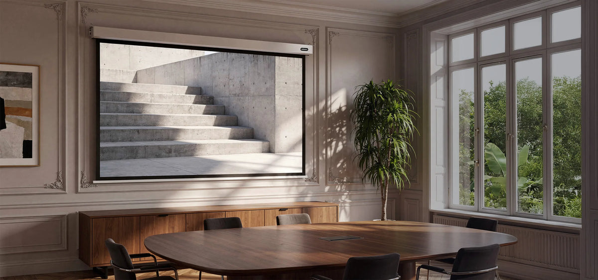 Elegant, well-lit meeting room. At the center of the scene, a large, extended celexon Professional Plus electric projection screen is mounted on the wall. Displayed on it is a minimalist architectural scene: light-colored concrete steps with clean geometric lines, intersected by natural light and striking shadows.