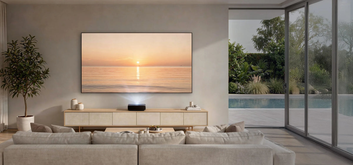 The image shows a modern, calm living room featuring a celexon CLR HomeCinema UST High Contrast Frame Projector Screen V2.0, displaying a warm sunset over the sea on a simple wall.