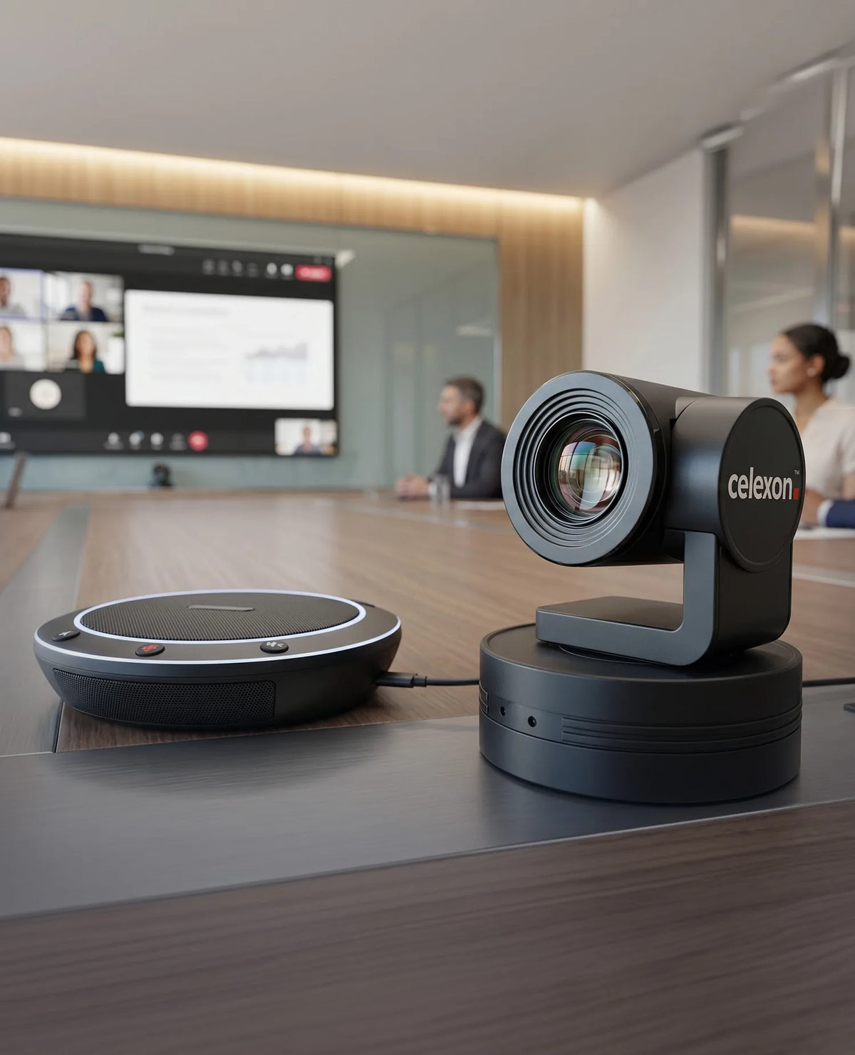 A modern conference room featuring a celexon VKS2040 video conferencing system on a meeting table; in the foreground are a pan-tilt conference camera and a speaker, while a screen in the background displays an ongoing video conference.