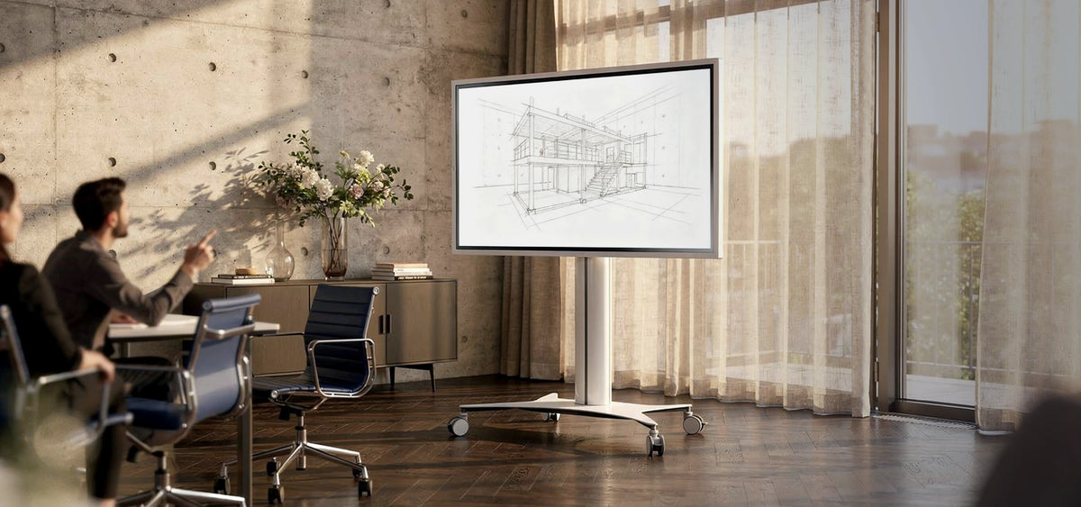 The image shows a modern office or creative studio with a celexon Seoul display trolley. On the screen, an architectural sketch of a building is displayed.